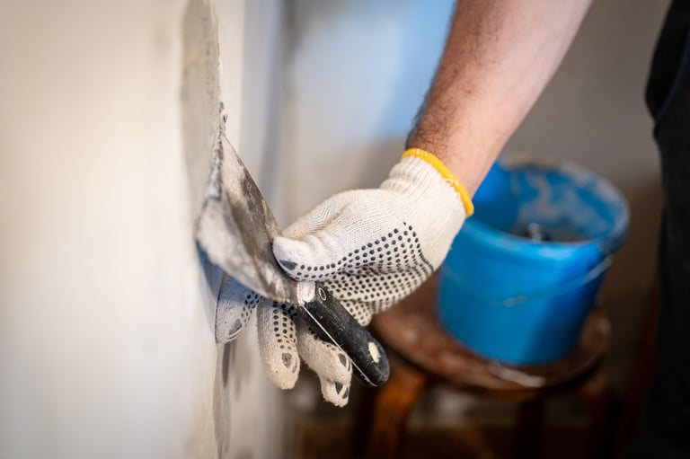 Worker's gloved hand pressing patching compound into a hole in an interior wall
